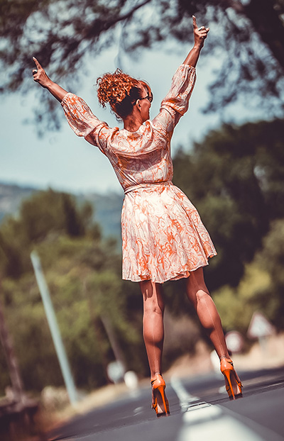 Femme de dos sur une route en robe estivale et bas couture en nylon, célébrant la liberté d'être femme